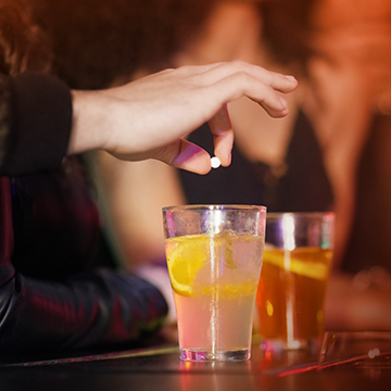 Photo of hand holding a pill over a drink.